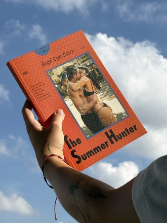 Mão segurando o livro The Summer Hunter contra o céu azul