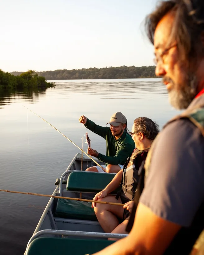 Grupo sentado na canoa ao entardecer, com a mata e o rio ao fundo
