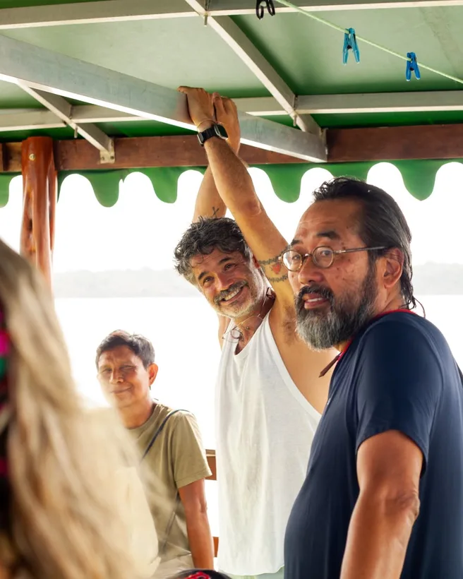 Três pessoas sob a cobertura verde do barco, uma delas alcançando o teto