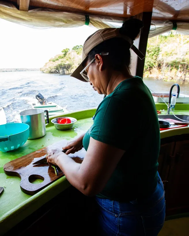 Mulher de camiseta verde preparando comida numa mesa no convés do barco
